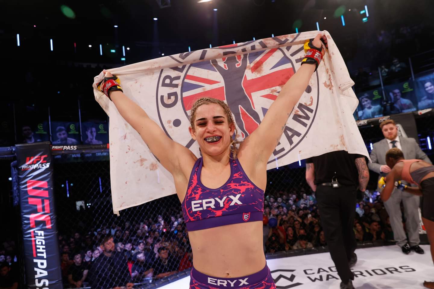 Kate Bacik celebrating a win in the cage, holding a Great Britain team flag above her head
