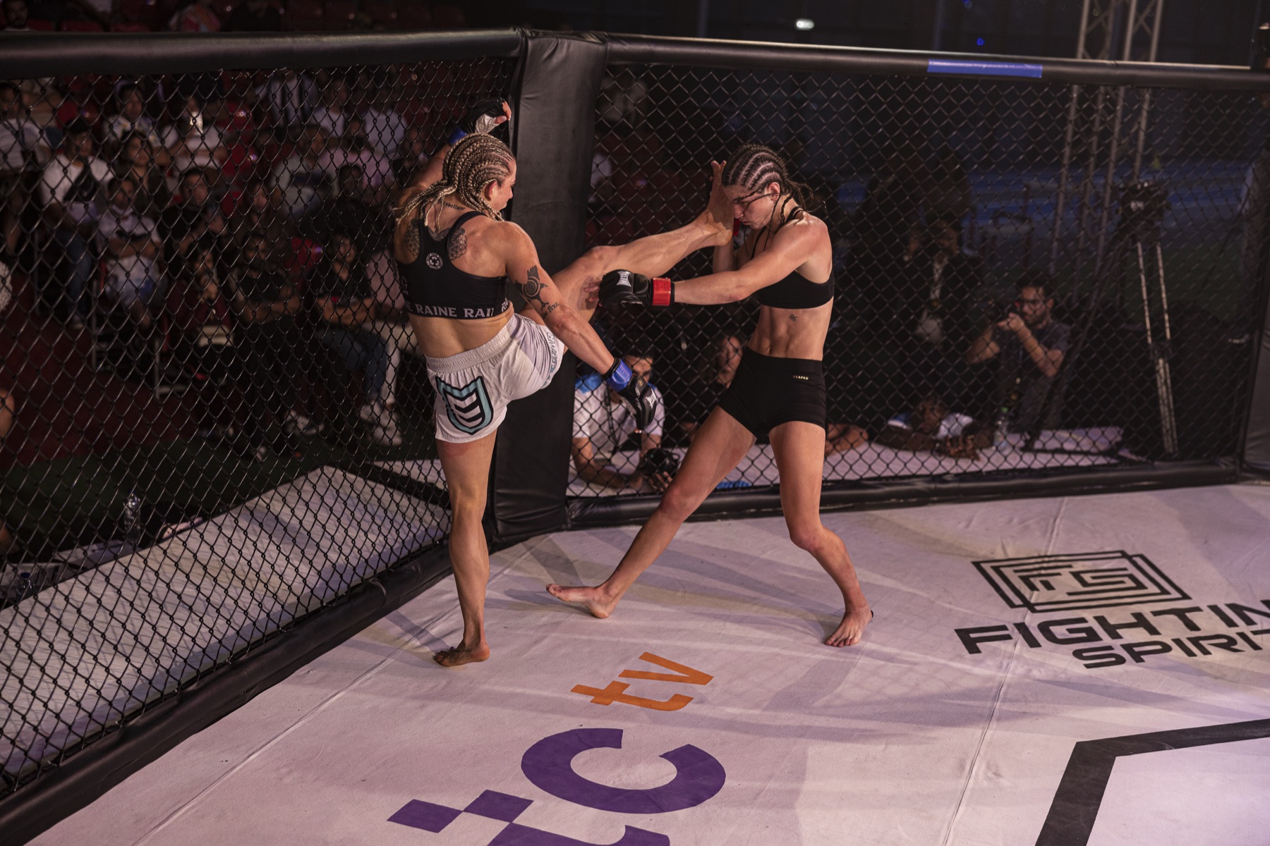Kate Bacik landing a high kick on her opponent against the cage